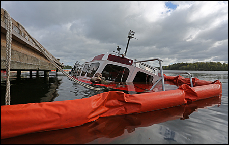 Räddningstjänstens länsor omgärdar fartyget som står på sjön Åsundens botten.